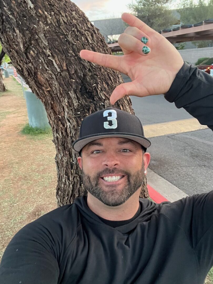image (913f168a-2c44-454b-9cea-40ed53ed632b) A man in black shirt and hat near tree.